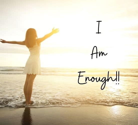 Woman on beach at sunset with arms spread "I am enough!!"