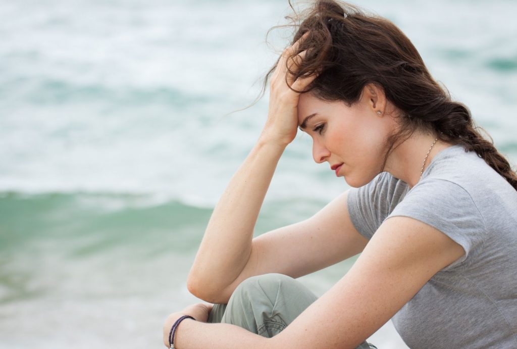 stressed woman sitting on beach looking pensive