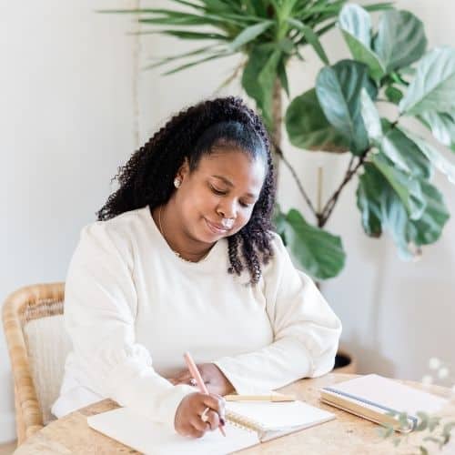 Woman of color sitting at kitchen table writing in a journal