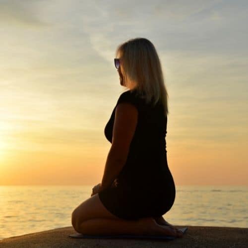 woman kneeling next to water at sunset.