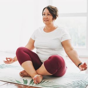 Self-care with meditation: woman on mat sitting cross legged for meditation.